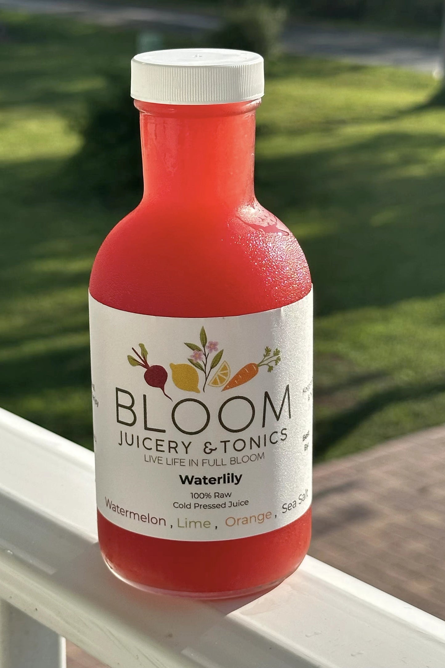 Bottle of Bloom Juicery & Tonics Waterlily juice on a ledge with grass in the background