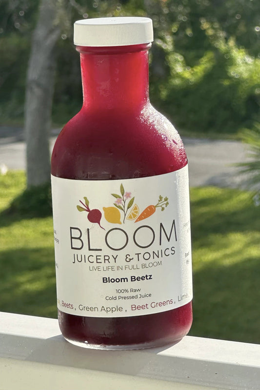 Bottle of Bloom Juicery & Tonics Beet juice with a blurred green outdoor background
